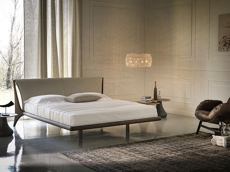 Upholstered bed with a pale wall, pendant light, rug and chair.