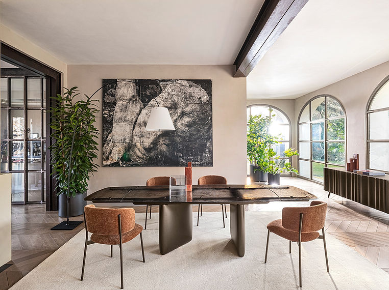 Dining table and upholstered chairs in a bright room with arched windows.