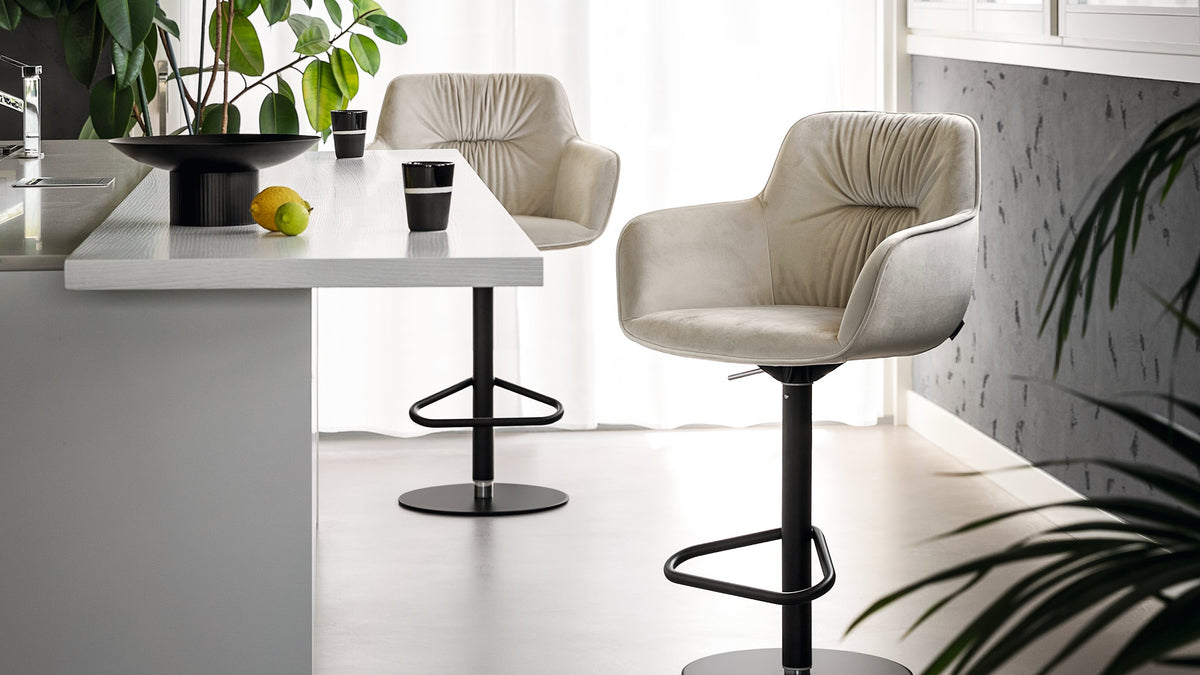 Calligaris Cocoon adjustable stools in light upholstery beside a kitchen island.