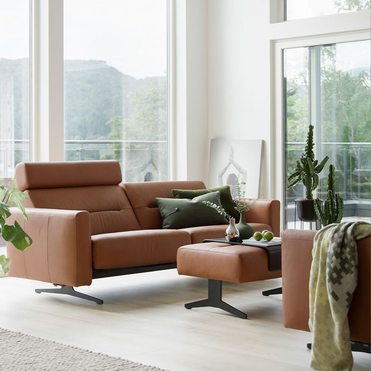 Stressless Stella seating in cognac leather beside large windows.