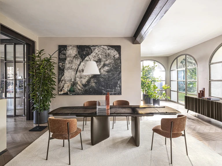 Calligaris Riverstone dining table with rust-coloured upholstered chairs in a bright room with arched windows.