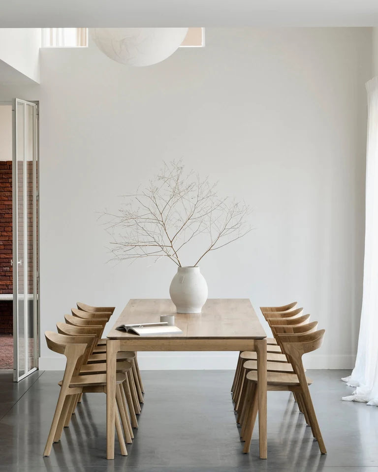 Ethnicraft oak Bok dining table and chairs with a vase of branches in a light-filled room.
