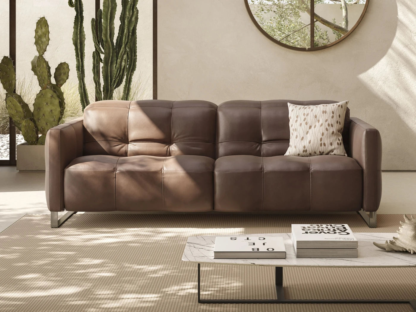 Brown Natuzzi Italia Philo sofa in a warm room with cacti, a circular mirror and a marble coffee table