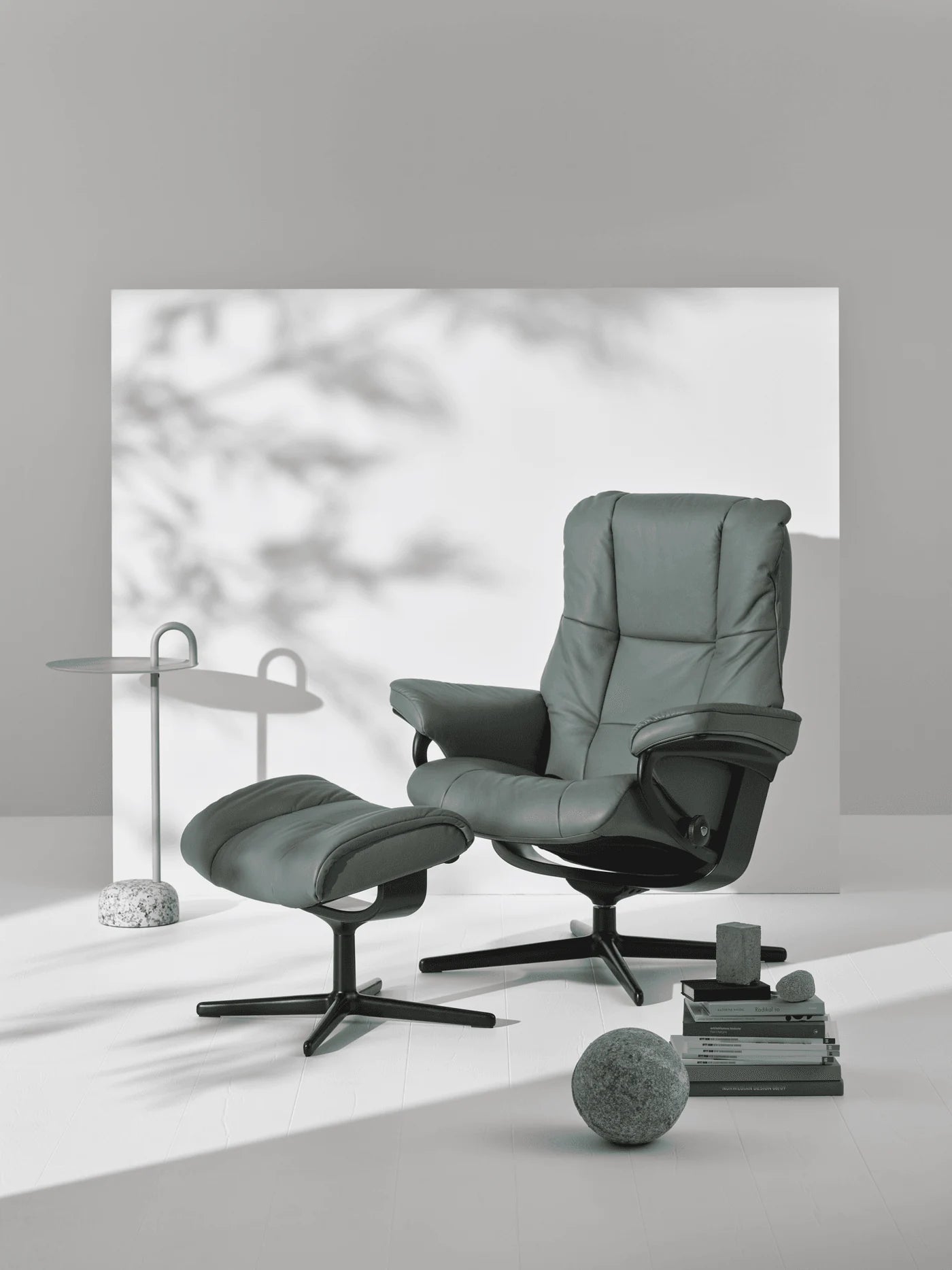 Stressless Mayfair Cross recliner and footstool in Paloma Sage Green leather with a black base in a softly lit room